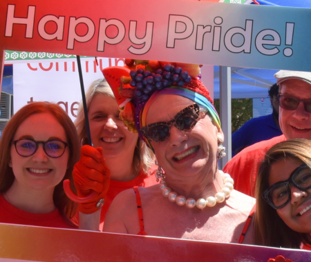 A person stands at a festival with a pride flag around their shoulders